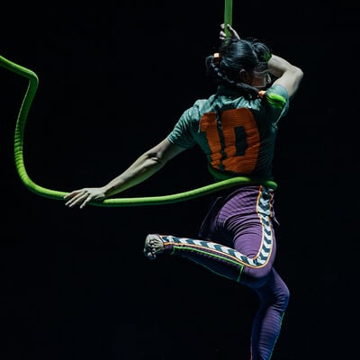 Artista vestido con ropa deportiva lleva el número diez en la espalda y se aferra a una cuerda verde - Messi10 Cirque du Soleil